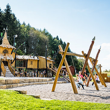 Das Bild zeigt Kinder, die auf de Spielplatz mit Rutschen, Schaukeln und Klettergerüsten spielen.