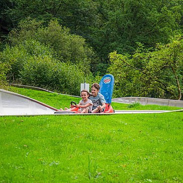 Das Bild zeigt zwei Kinder, die die Sommerrodelbahn beim Freizeitzentrum Peterberg fahren.